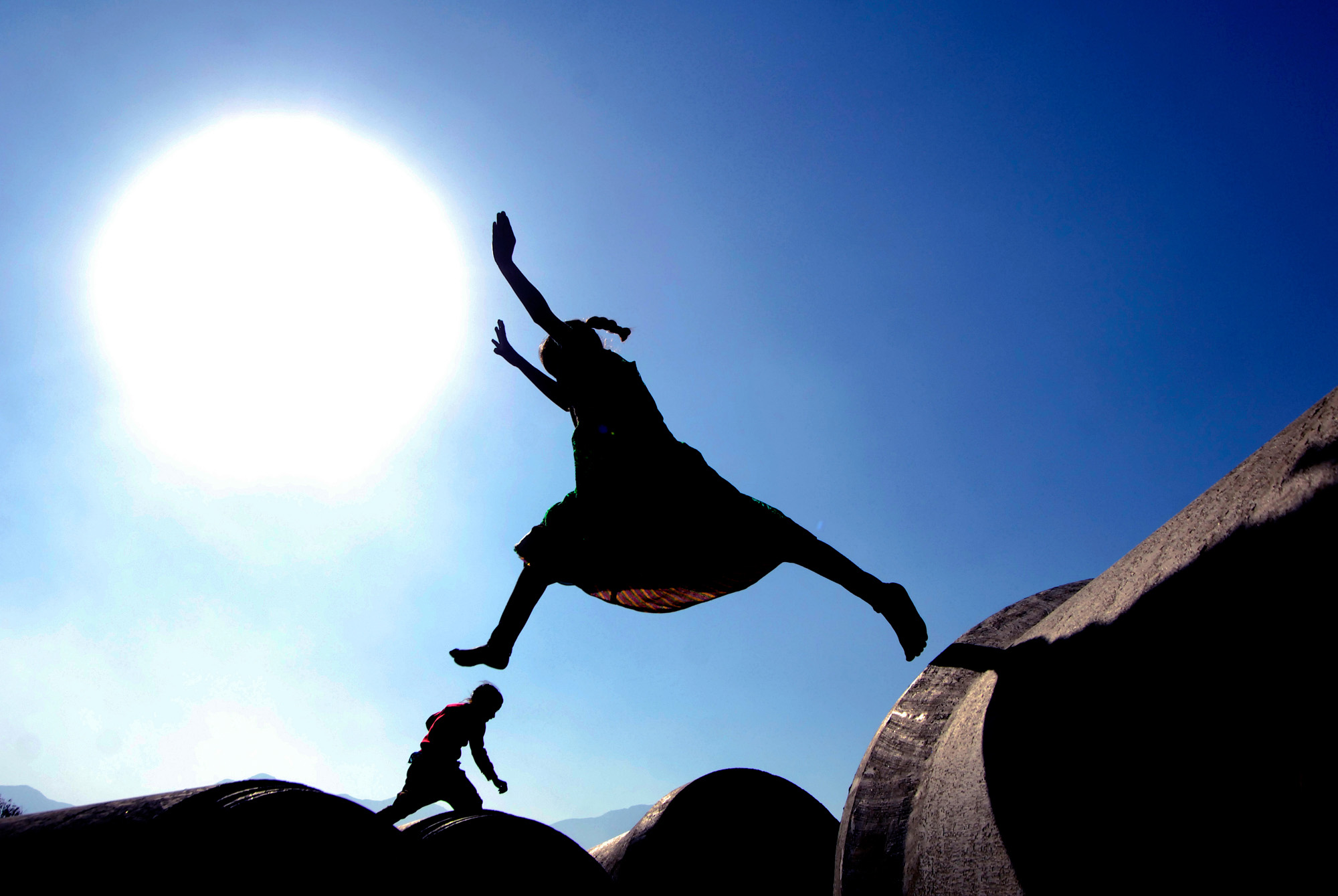 A girl jumps on top of sewage pipes.